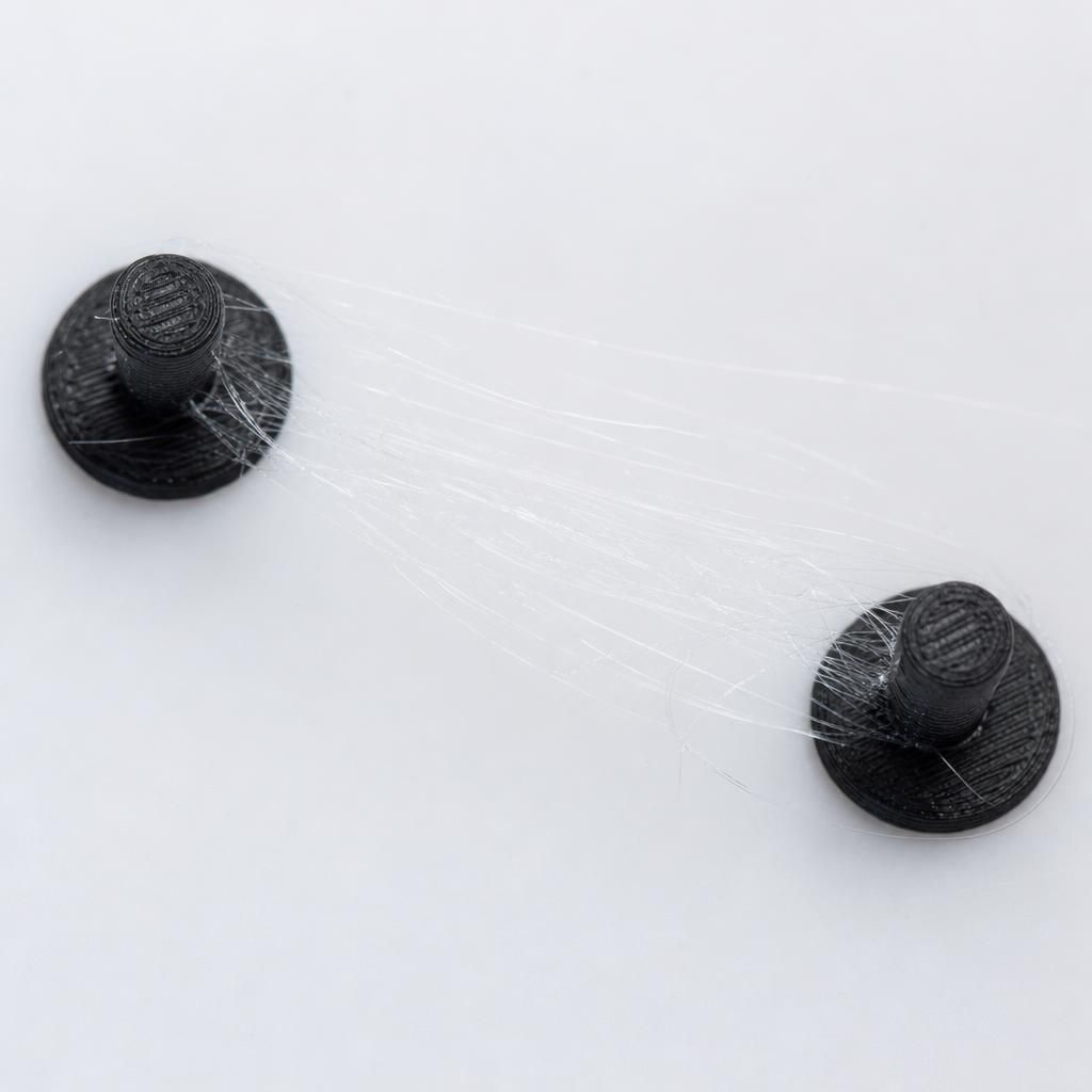 Detalhe de fios de stringing na impressão 3D esticados entre dois pinos da peça