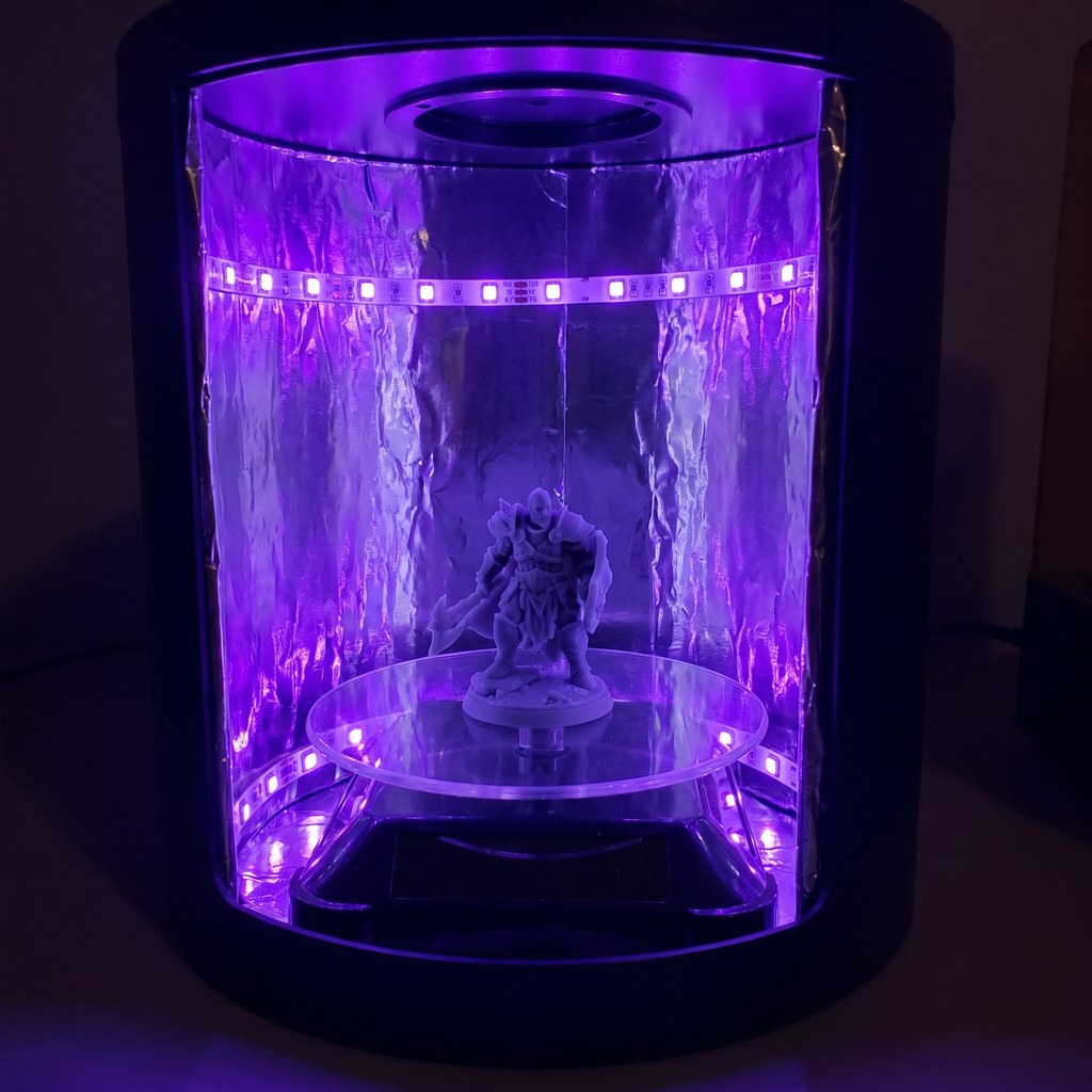 Peça de resina impressa em 3D curando sob luz UV violeta dentro de uma estação de cura